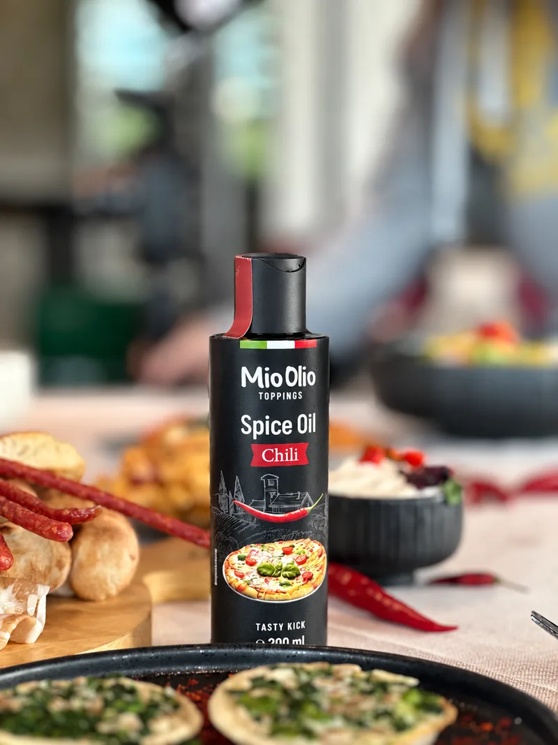 MioOlio Chiliöl in der Squeeze-Flasche auf einem gedeckten Tisch mit frischen Chilis